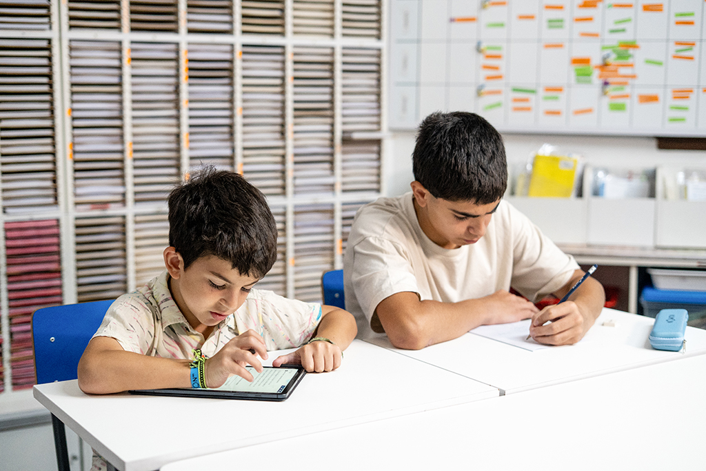 Dos estudiantes en un aula de Kumon, uno trabajando en una tableta y otro escribiendo en papel