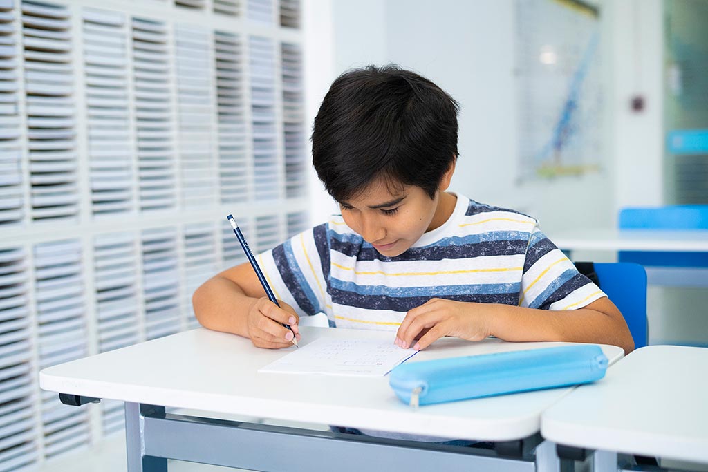 Niño concentrado resolviendo ejercicios en papel como parte del método de estudio individualizado de Kumon